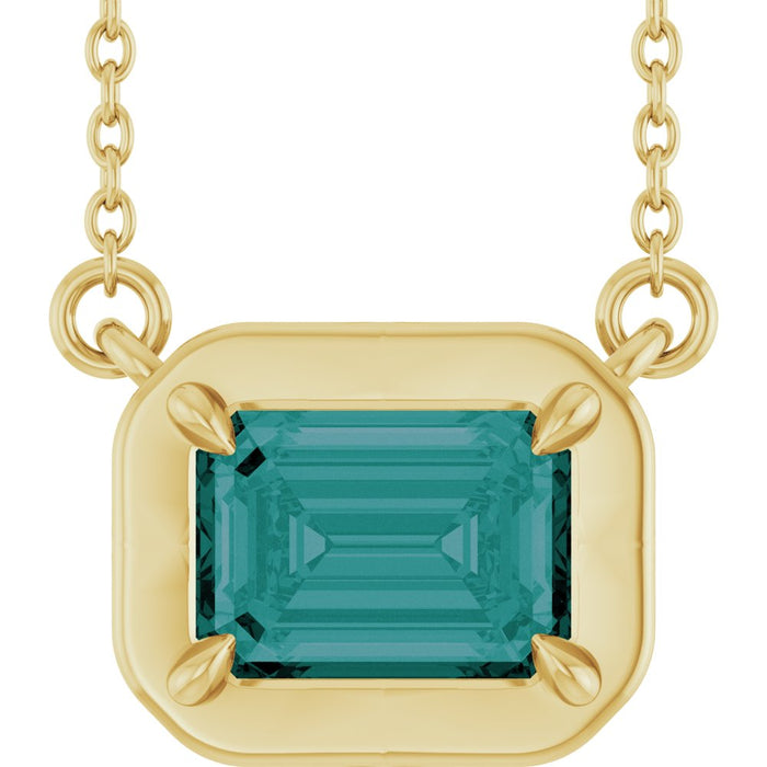 Gold necklace with a green gemstone pendant on a white background
