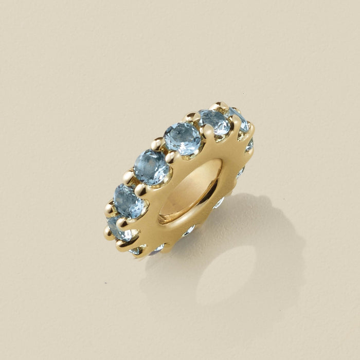 Gold slider charm with blue gemstones on a beige background