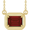 Gold necklace with a red gemstone pendant on a white background