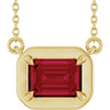 Gold necklace with a red gemstone pendant on a white background