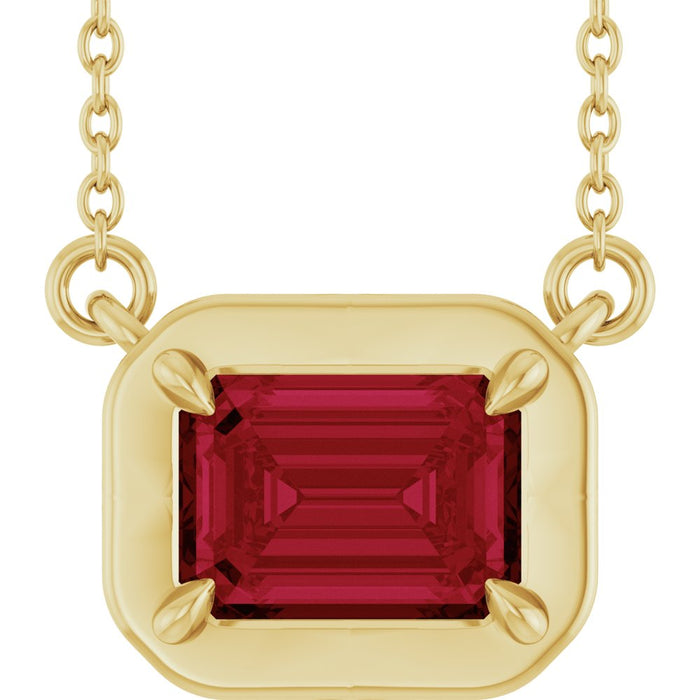 Gold necklace with a red gemstone pendant on a white background