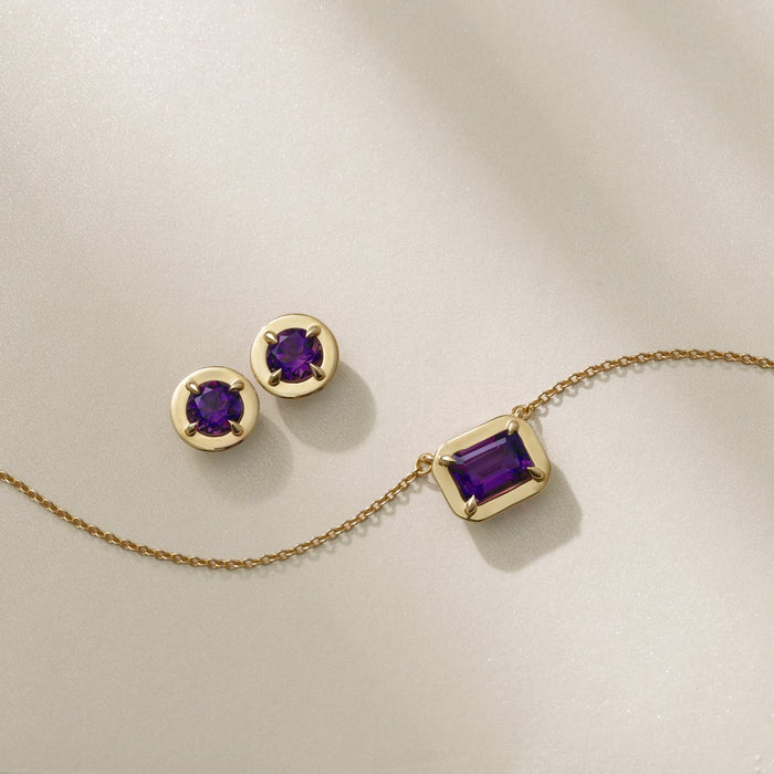 Gold necklace and earrings with purple gemstones on a light green background