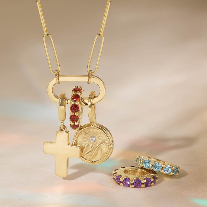 Gold necklace with various charms and slider pendants on a soft beige background