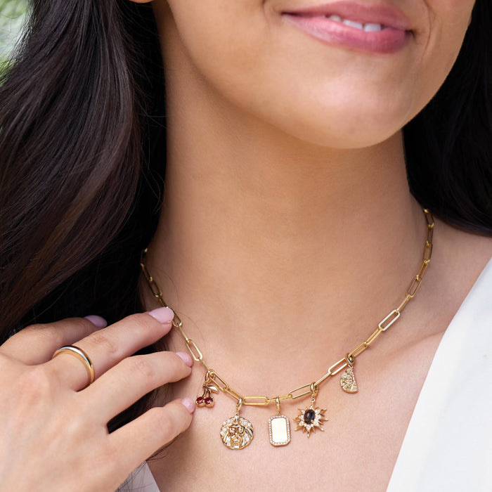 Close-up of a woman wearing a gold necklace with charms, outdoors.