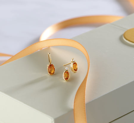Pair of gold earrings with orange gemstones on a light green surface.