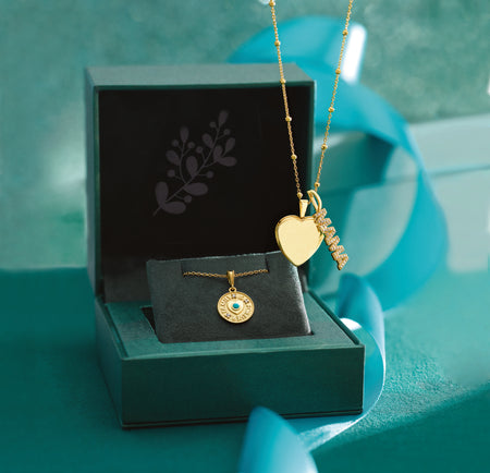 Gold necklaces with heart and 'MAMA' diamond pendants in a green box on a green background