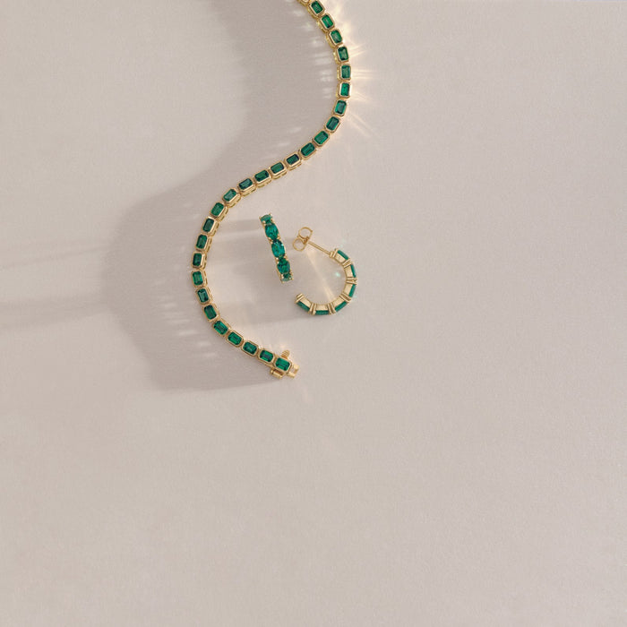 Gold necklace with green emerald gemstones on a light gray background