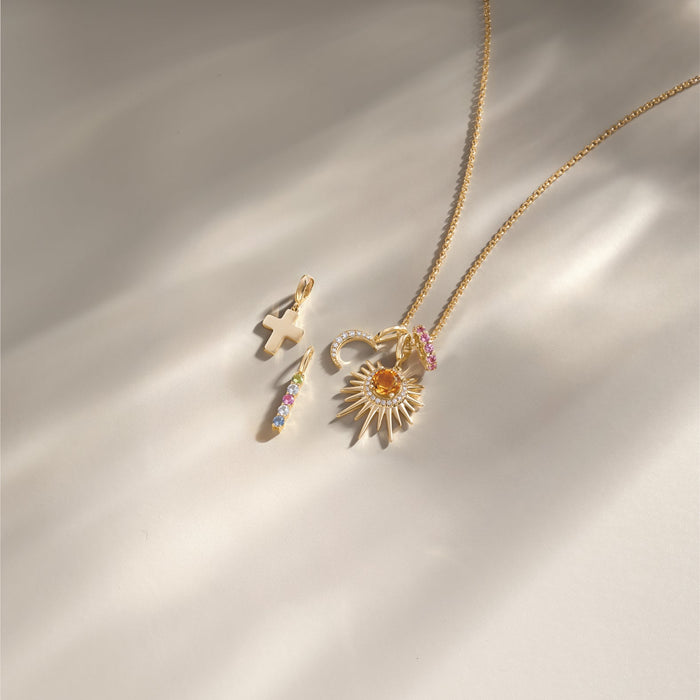 Gold necklace with sun pendant and charms on a light green background