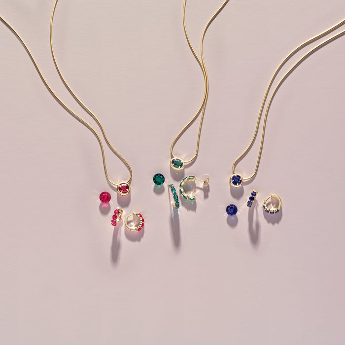 Gold necklaces with gemstone pendants on a light gray background