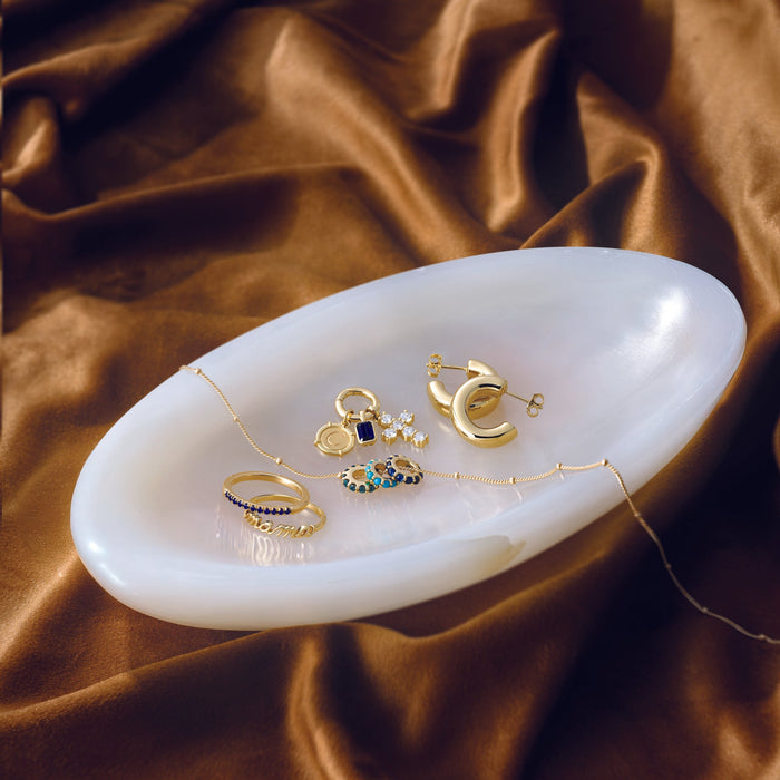 Gold jewelry including rings and earrings on a white dish with a brown fabric background