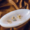 Gold jewelry including rings and earrings on a white dish with a brown fabric background
