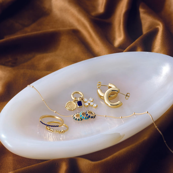 Gold jewelry including rings and earrings on a white dish with a brown fabric background