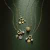 Charm necklaces with paperclip style gold links and different shaped charm bails with gemstone charms on a green background.
