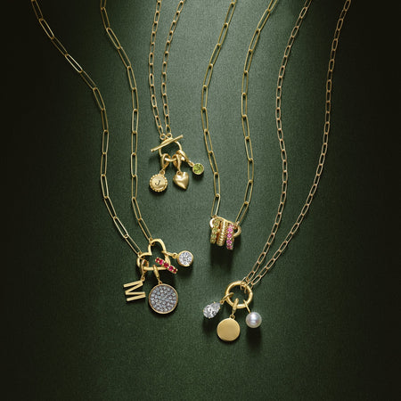 Charm necklaces with paperclip style gold links and different shaped charm bails with gemstone charms on a green background.