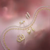 Gold jewelry set including necklace, earrings, and ring on a pink floral background