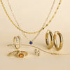 Gold jewelry including necklaces, rings, and hoop earrings on a beige background