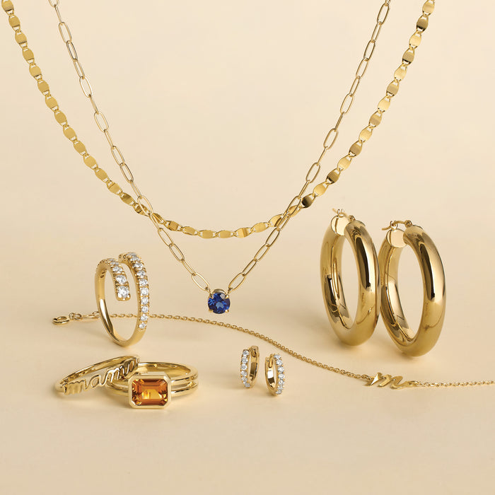 Gold jewelry including necklaces, rings, and hoop earrings on a beige background