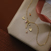 Gold necklace with charms on a beige box with a red ribbon