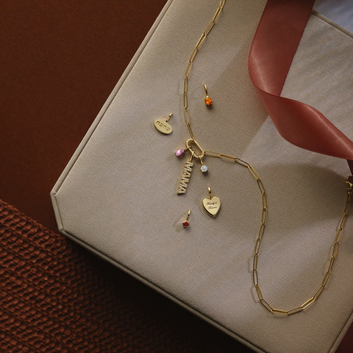Gold necklace with charms on a beige box with a red ribbon