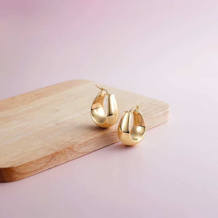 Gold earrings on a wooden board with a pink background