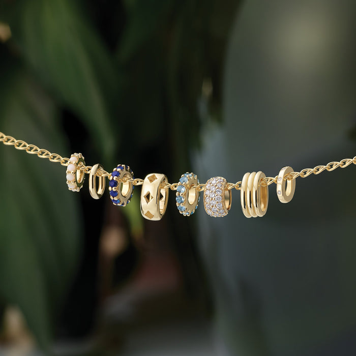 Gold necklace with various slider gemstone charms on a blurred green background
