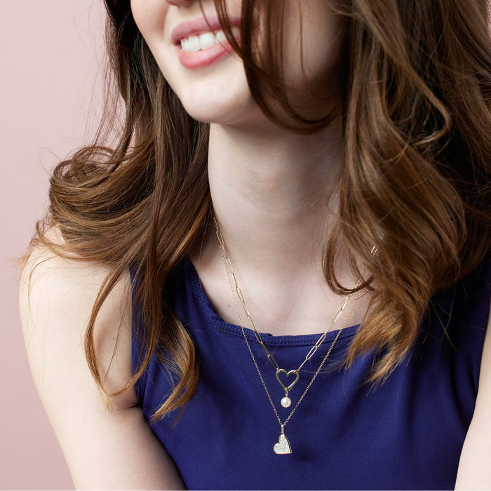 Woman wearing gold paperclip heart bail charm necklace with pearl charm. 