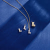 A gold chain necklace with three letter 'L' pendants, each adorned with floating diamond initials, displayed on a textured dark blue fabric background.