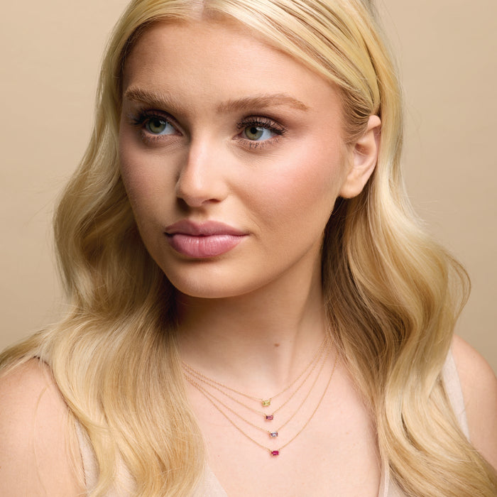 Woman with long blonde hair and pink lipstick against a beige background wearing birthstone necklaces