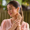 Woman in a pink dress adjusting her earrings with a blurred green background