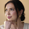 Woman wearing gold earrings and bracelet against a beige background
