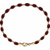 A gold tennis bracelet featuring oval-cut deep red garnet gemstones, arranged in a circular shape on a solid white background.