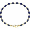 A yellow gold tennis bracelet featuring oval-cut dark blue gemstones, arranged in a circular shape on a plain white background.