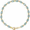 A yellow gold tennis bracelet featuring a row of light blue oval cut sky blue topaz gemstones, displayed on a clean white background.
