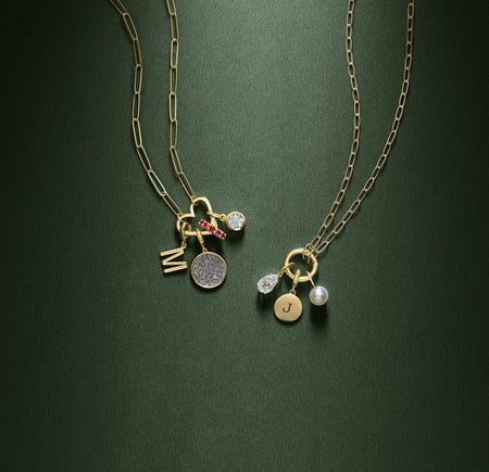 Two paperclip style gold charm necklaces with charm bails on a green background.