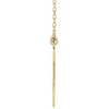 Side view of gold graduation diamond necklace with a long, thin pendant on a white background