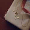 Gold necklace with charms on a beige box with a red ribbon