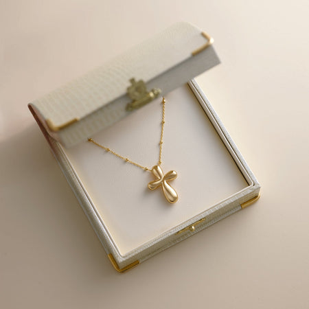 Gold necklace with a cross pendant in an open jewelry box on a light background