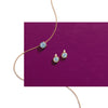 A gold chain necklace and matching stud earrings with round light blue gemstones, arranged on a solid magenta rectangular card against a white background.
