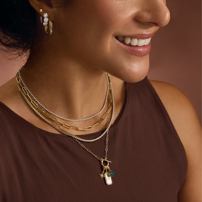Woman wearing multiple gold necklaces with a brown shirt.