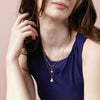 Woman wearing gold paperclip heart bail charm necklace with pearl charm. 