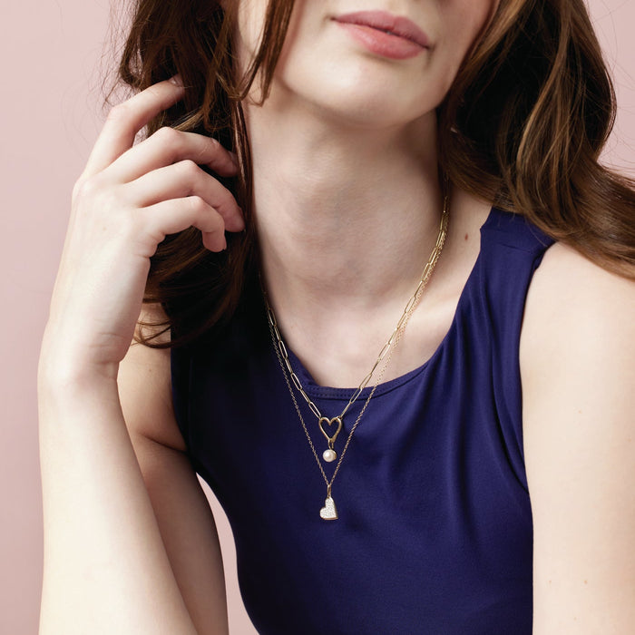 Woman wearing gold paperclip heart bail charm necklace with pearl charm. 