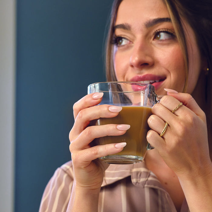 Woman wearing gold 'mama' script ring holding a glass of iced coffee against a plain background