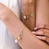 Gold bracelets with charms on a person's wrist against a neutral background