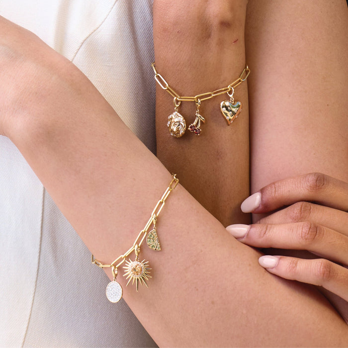 Gold bracelets with charms on a person's wrist against a neutral background