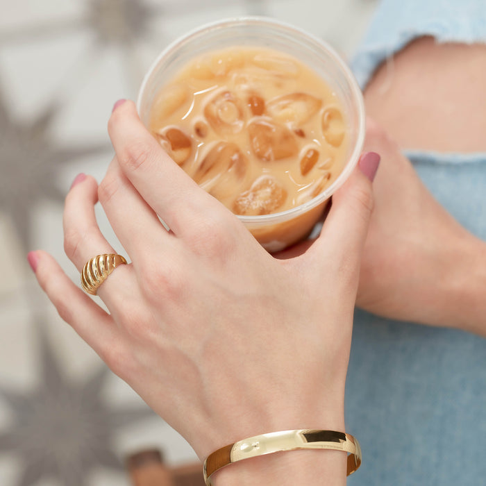 Model drinking iced coffee wearing bold gold chunky ring and bangle bracelet
